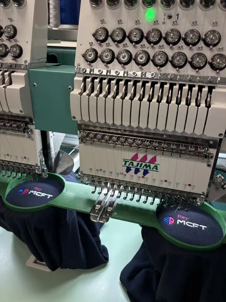 Multi-head embroidery machine stitching MCFT-branded logos on dark fabric.
