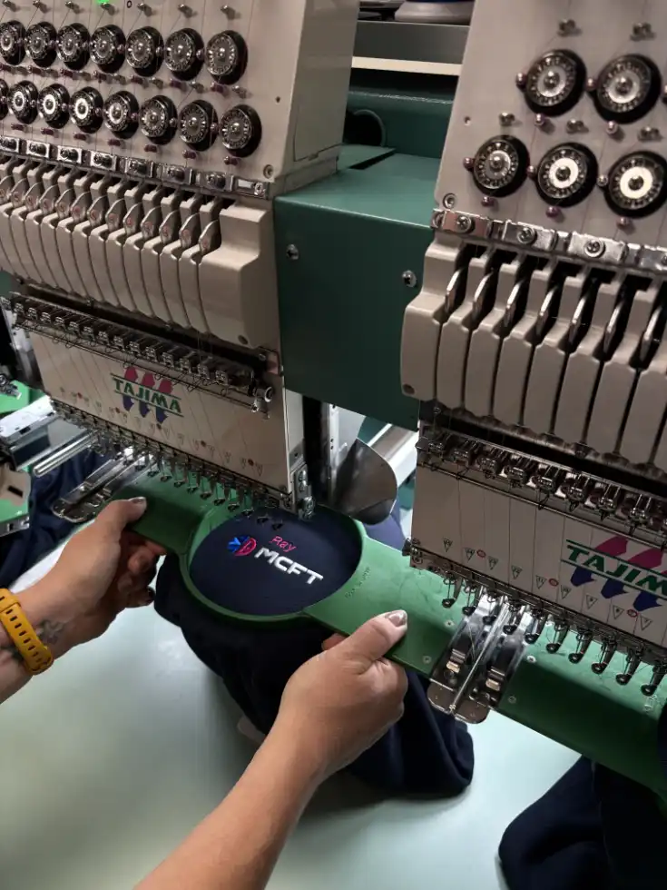 Hands setting up a polo shirt for logo embroidery on an industrial embroidery machine.