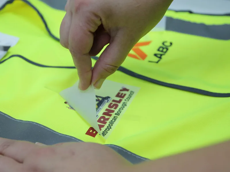 DTF transfer film being peeled off a freshly printed logo on a hi vis vest